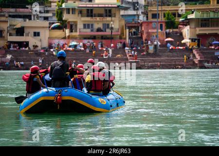 amici in famiglia seduti in zattera per praticare sport d'avventura mentre attraversano di fronte al ghat e al tempio sulle rive del fiume santo ganga Foto Stock