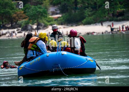 amici in famiglia seduti in zattera per praticare sport d'avventura mentre attraversano di fronte al ghat e al tempio sulle rive del fiume santo ganga Foto Stock