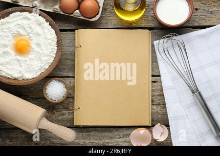 Libro di ricette in bianco circondato da diversi ingredienti su tavolo di legno, piatto. Spazio per il testo Foto Stock