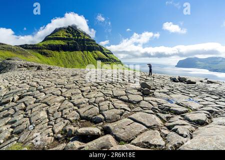 Un turista che fotografa la montagna di Skaelingsfjall in piedi sul terreno incrinato in estate, l'isola di Streymoy, le isole Faroe, la Danimarca, l'Europa Foto Stock
