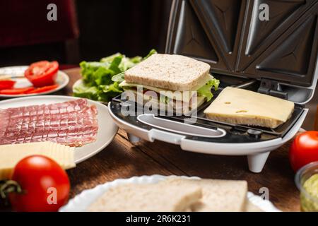 Cottura di panini con farciture diverse. Paninoteca e vari ingredienti su sfondo di legno. Foto Stock