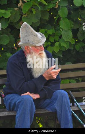 Vecchio uomo sulla panca del parco che fuma pipa, barba piena Foto Stock