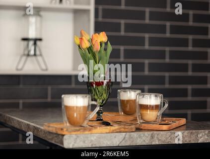 un bouquet di tulipani rosso-arancio e una tazza di caffè caldo sono sul tavolo Foto Stock