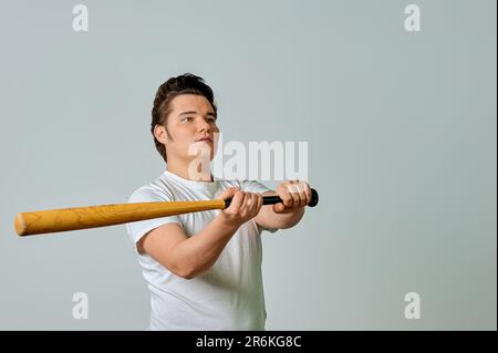 Un uomo con un pipistrello in mano oscilla su uno sfondo grigio Foto Stock