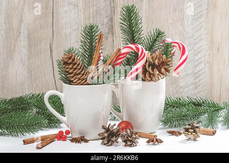 Durante le festività natalizie, con due tazze di caffè in ceramica bianca e una serie di coni di pino, bastoncini di cannella e fogliame decorativo Foto Stock