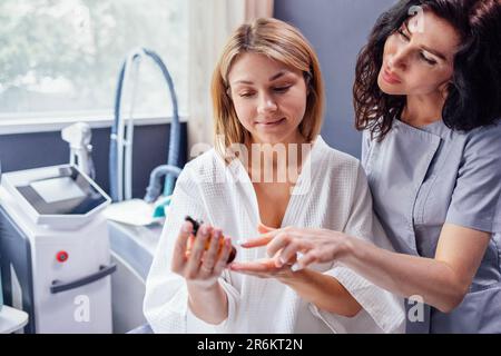 Bella estetista caucasica comunica con la sua cliente femminile. Il padrone di bellezza tiene i cosmetici nelle sue mani e li mostra a donna blod. Apparato fo Foto Stock