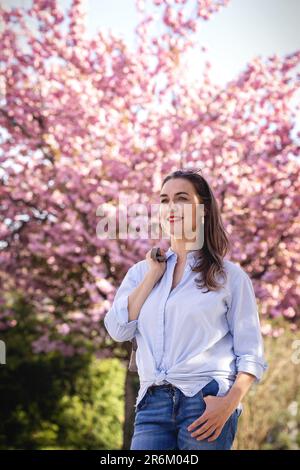 Bella donna sorridente sullo sfondo di fiori di ciliegio lilla rosa Foto Stock