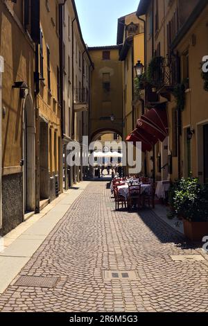 Vicolo in parte all'ombra con tavoli e sedie di un ristorante in una giornata di sole in una città italiana Foto Stock