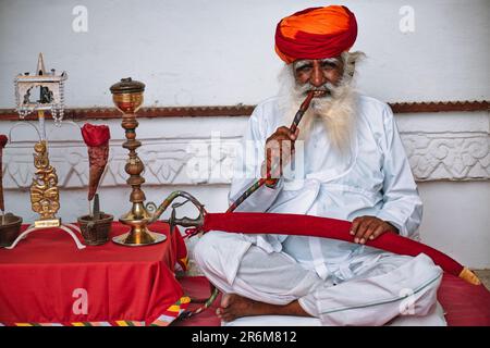 Il vecchio uomo indiano fuma hookah (pipa d'acqua) nel forte di Mehrangarh Foto Stock