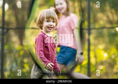 Carino bambino ragazzo e sua sorella saltando su un trampolino in un cortile. Sport ed esercizi per bambini. Attività estive all'aperto. Foto Stock