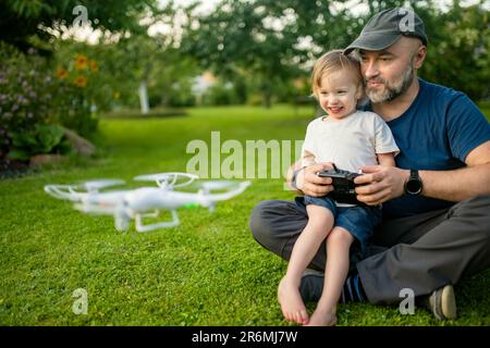 Padre e figlio guardano e navigano in un drone. Carino bambino ragazzo aiutando suo padre ad azionare un drone da telecomando. Tempo libero per tutta la famiglia. Foto Stock