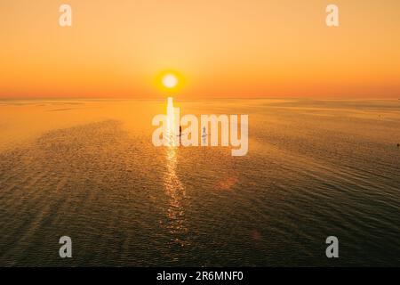 Vista aerea di due persone su tavole stand up paddle sul mare tranquillo al tramonto. Vacanza calda estate sulla spiaggia. Tempo libero attivo sul mare. Foto Stock