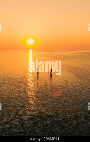 Vista aerea di due persone su tavole stand up paddle sul mare tranquillo al tramonto. Vacanza calda estate sulla spiaggia. Tempo libero attivo sul mare. Foto Stock