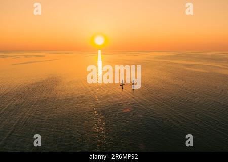 Vista aerea di due persone su tavole stand up paddle sul mare tranquillo al tramonto. Vacanza calda estate sulla spiaggia. Tempo libero attivo sul mare. Foto Stock