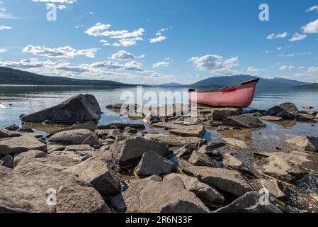 Vista estiva nel nord del Canada con vista sul lago e sulle montagne. Canoa rossa in vista a fuoco. Foto Stock