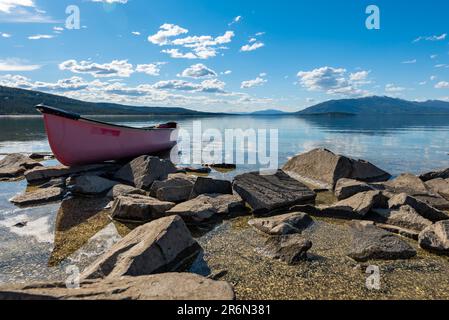 Vista estiva nel nord del Canada con vista sul lago e sulle montagne. Canoa rossa in vista a fuoco. Foto Stock