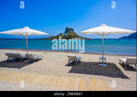 Sdraio e ombrellone sulla bellissima spiaggia di Agios Stefanos di fronte al paradiso isola Kastri - rovine storiche e scenario paradiso sulla costa dell'isola Foto Stock