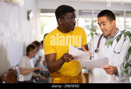 Medico positivo che consulta il paziente afro-americano circa il trattamento prescritto Foto Stock