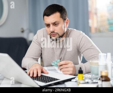 Giovane uomo in cerca di informazioni sui medicinali sul portatile Foto Stock