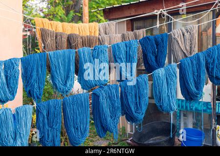 Matasse di filo tinto a mano nelle sfumature di blu, oro e taupe appendono su linee di corda per asciugare all'aperto al negozio di tessitura Trujillo a Chimayo, New Mexico. Foto Stock