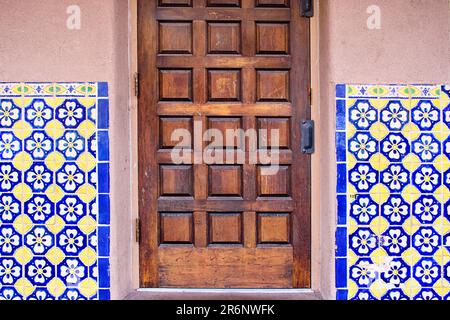 Immagine orizzontale di una tradizionale piastrella dipinta a mano di giallo, blu e bianco su una parete di stucco che circonda una porta di legno marrone a Santa Fe, New Foto Stock