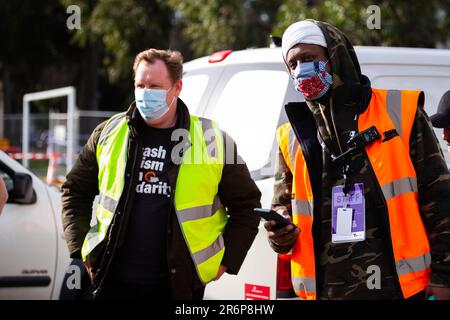 MELBOURNE, AUSTRALIA - LUGLIO 10: Il Segretario del Consiglio Victorian Trades Hall, Luke Hilakari (a sinistra) guarda con un lavoratore del governo (a destra) mentre un camion pieno di carne arriva ad Alfred Street durante il COVID 19 il 10 luglio 2020 a Melbourne, Australia. L'ex leader federale del lavoro Bill Shreen, insieme a stretti alleati al Trades Hall aiutano a consegnare la carne Halal, fornita dalla Macca Halal Foods alle torri della commissione per gli alloggi bloccati dopo un'epidemia di COVID-19 rilevata all'interno del complesso. Il signor Shrear ha potuto usare il suo alto profilo per garantire che il cibo non sia stato allontanato dalla polizia in modo che raggiungesse la r Foto Stock