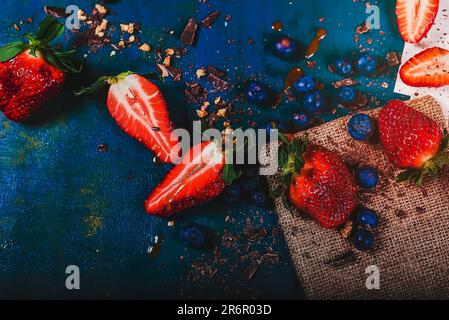 Una foto di fragole appena raccolte e gocce di cioccolato fondente su sfondo blu Foto Stock