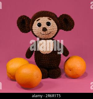 Giocattolo bambino morbido maglia marrone Cheburashka su rosa . Concetto DIY. Lavoro fatto a mano. Hobby cucire e lavorare a maglia con fili di lana. Carattere Foto Stock