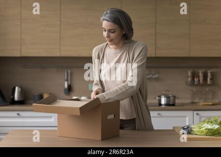 Cliente maturo positivo donna disimballaggio pacco, pacchetto di apertura Foto Stock