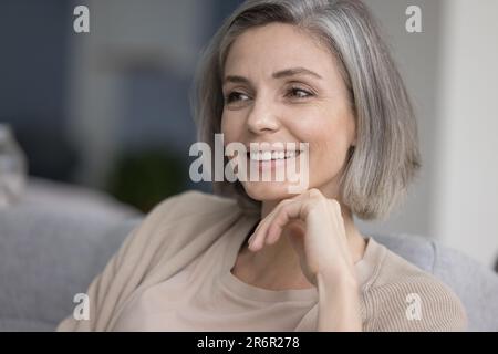 Felice donna dai capelli grigi graziosi che si rilassa sul divano a casa Foto Stock