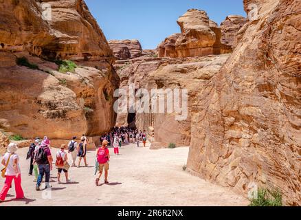 I turisti camminano verso il Siq, la stretta gola che è l'ingresso principale che conduce al Tesoro e l'antica città di Petra, in Giordania. Foto Stock