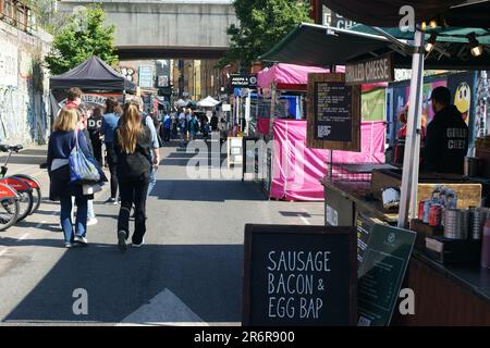 Street View di Brick Lane con giovani hipsters e turisti a piedi. Street Art graffiti murali in background. Brick Lane, Shoreditch, London, Regno Unito Foto Stock