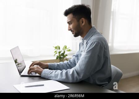 Un giovane dipendente indiano impegnato e positivo si è concentrato sul lavoro Foto Stock