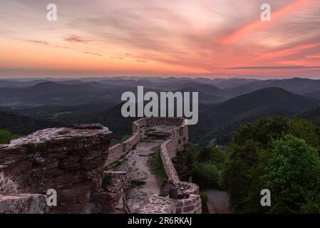 Una giovane coppia si siede sulle rovine del castello di Wegelnburg guardando l'alba colubre sui Monti Palatinati in primavera, Renania-Palatinato, Germania Foto Stock