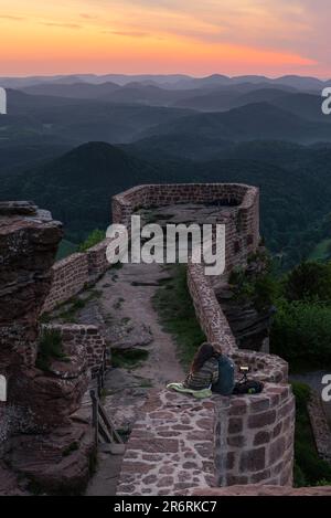Una giovane coppia si siede sulle rovine del castello di Wegelnburg guardando l'alba colubre sui Monti Palatinati in primavera, Renania-Palatinato, Germania Foto Stock