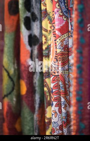 Tessuti di lana tessuti con diversi motivi colorati più in tonalità rosse appesi per la vendita in un negozio, spazio copia, fuoco selezionato, profondità molto stretta di fiel Foto Stock