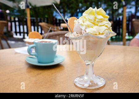 Gelati in una ciotola di vetro e una tazza di caffè sul tavolo in un caffè all'aperto, delizioso dolce e rinfresco in estate, focus selezionato, Foto Stock