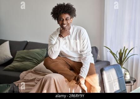 Giovane ragazzo afro-americano di gen z sorridente seduto sul divano a casa. Foto Stock