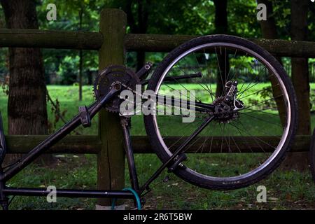 Bici rotta appoggiata su una recinzione di legno in un parco al tramonto Foto Stock