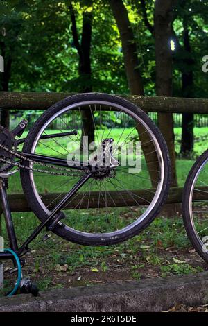 Bici rotta appoggiata su una recinzione di legno in un parco al tramonto Foto Stock