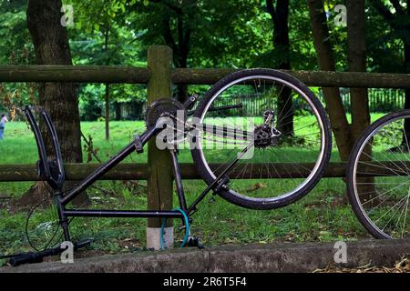 Bici rotta appoggiata su una recinzione di legno in un parco al tramonto Foto Stock