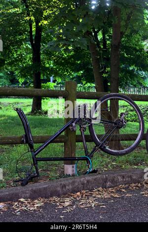 Bici rotta appoggiata su una recinzione di legno in un parco al tramonto Foto Stock