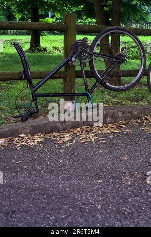 Bici rotta appoggiata su una recinzione di legno in un parco al tramonto Foto Stock