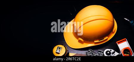 Giornata di lavoro o concetto di sicurezza sul lavoro, casco di sicurezza e utensili su sfondo scuro con spazio per le copie. Foto Stock