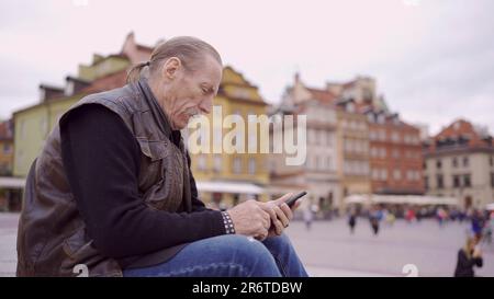 Varsavia, Polonia. 11th giugno, 2023. Senior si siede sulla scalinata e utilizza uno smartphone nel centro storico di una vecchia città europea. Piazza del Palazzo, Città Vecchia di Varsavia (Credit Image: © Andrey Nekrasov/ZUMA Press Wire) SOLO PER USO EDITORIALE! Non per USO commerciale! Foto Stock