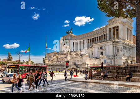 Persone che attraversano la strada a Piazza Venezia di fronte al monumento Vittorio Emanuele 11, un grande monumento nazionale in marmo bianco a Roma Foto Stock