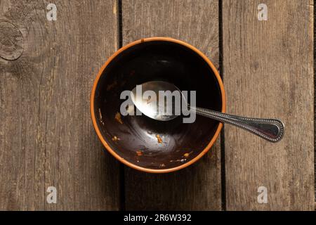 piatto marrone sporco dopo il pasto e cucchiaio sul vecchio tavolo di legno primo piano Foto Stock