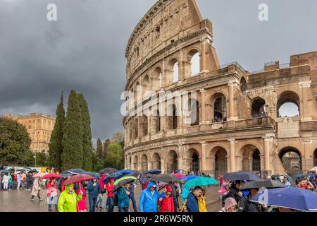 Persone con ombrelloni che visitano il Colosseo Romano durante le forti piogge e i cieli bui e tempestosi , Roma, Italia Foto Stock