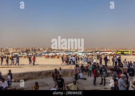 I turisti che arrivano in pullman all'Altopiano di Giza per visitare le piramidi, con il paesaggio urbano del Cairo sullo sfondo Foto Stock