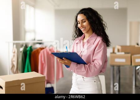 Fidato Businesswoman organizzare e imballare gli ordini di vestiti in Showroom elegante Foto Stock